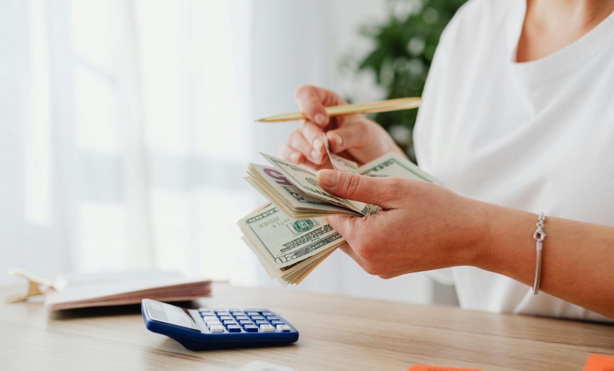 Persona contando dinero y realizando cálculos con una calculadora, imagen relacionada con el salario básico unificado 2026 en Ecuador.